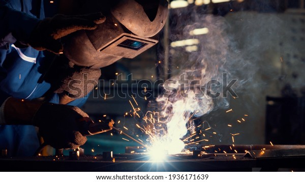 Skillful metal worker working with arc welding\
machine in factory while wearing safety equipment. Metalwork\
manufacturing and construction maintenance service by manual skill\
labor concept.