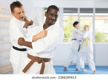 Skillful middle-aged male judo practitioner engaged in wrestling with his opponent during workout session - Powered by Shutterstock