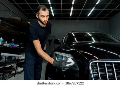 Skillful And Professional Male Auto Service Worker Polishing And Detailing A Car Body, Waxing Car Hood And Headlight With A Wax Or Nano Ceramic Coating. Car Wash Service.