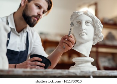 Skillful sculptor makes professional restauration of gypsum sculpture of woman's head at the creative workshop.