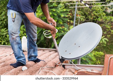 Skillful worker installing satellite dish and television antenna on roof top