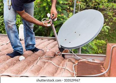 Skillful worker installing satellite dish and television antenna on roof top
