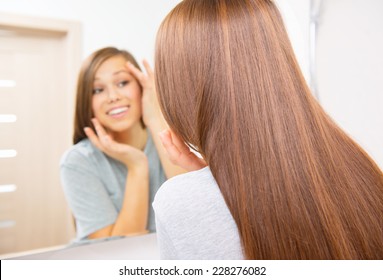 Skin care. Beautiful teenage girl checking her face before the mirror, admiring herself, enjoying her clean skin. Beauty woman touching her cheek, smiling. Perfect skin. Fresh Clean Skin. Skincare 