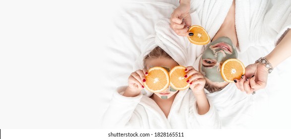 Skin care, beauty, spa. mother and daughter in white bathrobes applying pieces of orange to their eyes, in a white bath towel, posing to camera at home, touching face. - Powered by Shutterstock