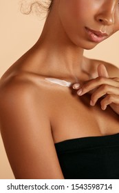 Skin care. Closeup woman's body with cosmetic cream on skin. Beautiful black girl with moisturizing lotion on hydrated body skin at studio