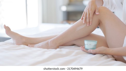Skin Care Concept - Close Up Of Lady Holds Cream Jar And Apply Lotion Onto Her Sexy Leg On Bed
