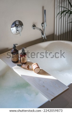 skin care cosmetics, cream in jar, body lotion and shower gel in brown bottles on bamboo caddy and water with bubble foam in bathtub at bathroom, detail in interior Foto stock © 
