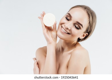 Skin care at home, sponge cleansing. Smiling girl on a white background with skin cleanser in her hands.