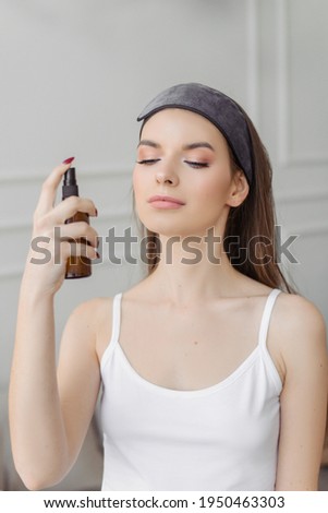 Skin care with moisturizing tonic. A young girl in a headband sprays hydrolate on her face.	