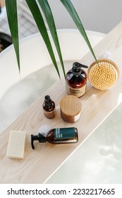 skin care products, natural cream in jar, body lotion in brown bottle, organic soap and massage peeling brush on bamboo caddy and bathtub with bubbles in bathroom, above view - Shutterstock ID 2232217665