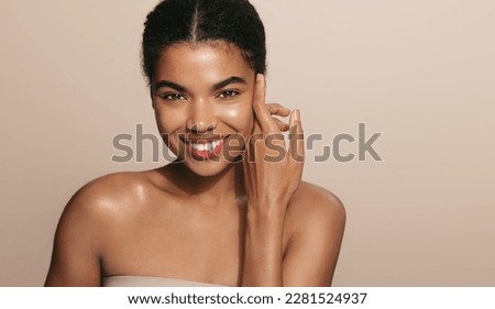 Skin care routine. Dark skinned woman with perfect glowing body, head and shoulders, touches her nourished face after skin cream and moisturizer, brown background.