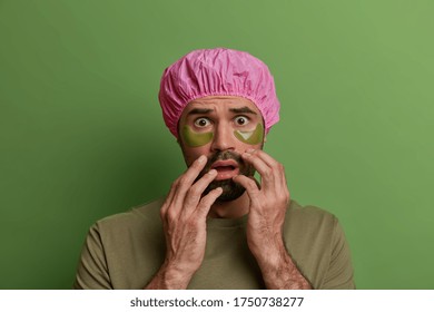 Skin Care Routine, Facial Treatment. Scared European Guy Wears Collagen Patches Under Eyes, Cares About Face, Wears Waterproof Shower Cap Dressed In Casual T Shirt Isolated On Bright Vivid Background.