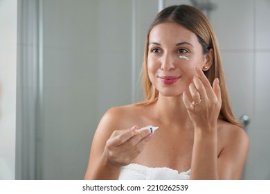 Skin care routine. Portrait of beautiful girl applying cream under eye with finger. Dark circles and anti-wrinkle concept. - Shutterstock ID 2210262539