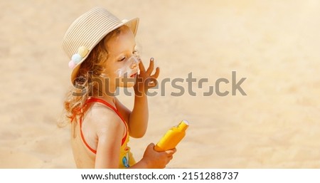 Skin care. Safe protection from the sun. Sunscreen for children. The child holds a bottle of moisturizing Sunscreen in his hands and puts a protective layer on his face.
