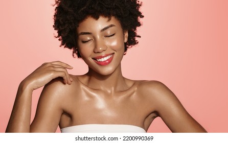 Skin care. Smiling African American beauty model, girl laughing and smiling, has shiny, clear glowing skin, body after shower, standing over pink background