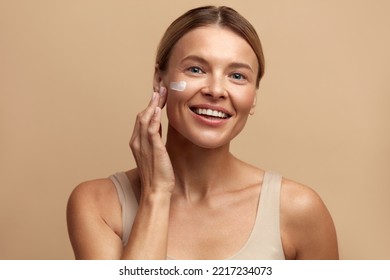 Skin Care Woman Applying Cream on Cheek. Closeup Of Beautiful Smiling Girl Putting Cream On Fresh Soft Pure Skin. Portrait Of Woman With Natural Makeup Applying Beauty Cosmetics Product 