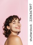 Skin care. Woman with beauty face and healthy facial skin portrait. Beautiful curly girl model with natural makeup touching glowing hydrated skin on pink background closeup. High quality image.