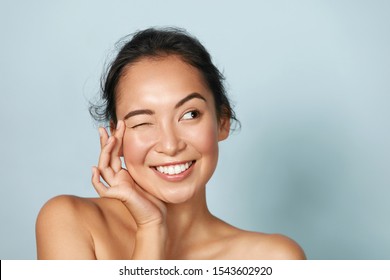 Hautpflege. Frauen mit SchönheitsGesicht, die gesundes Gesichtsporträt berühren. Schönes, lächelndes asianisches Mädchenmodell mit natürlicher Schminke, die leuchtend hydrierte Haut auf blauem Hintergrund Nahaufnahme
