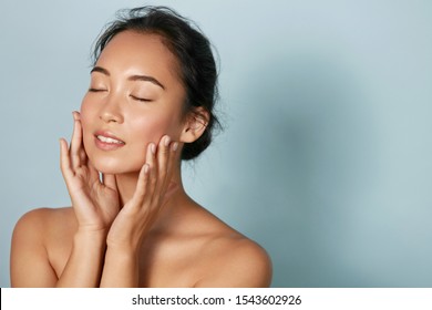 Skin care. Woman with beauty face and healthy facial skin portrait. Beautiful asian girl model with natural makeup touching glowing hydrated skin on blue background closeup. High quality image - Shutterstock ID 1543602926