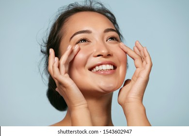  Hautpflege. Frauen mit SchönheitsGesicht, die gesundes Gesichtsporträt berühren. Schönes, lächelndes asianisches Mädchenmodell mit natürlicher Schminke, die leuchtend hydrierte Haut auf blauem Hintergrund Nahaufnahme