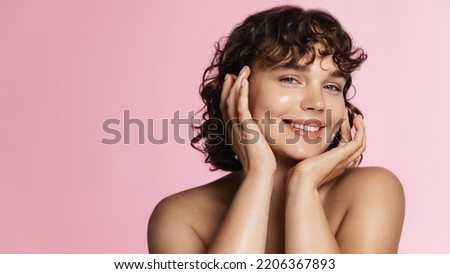 Skin care. Woman with beauty face touching healthy facial skin portrait. Beautiful smiling girl model with natural makeup touching glowing hydrated skin on pink background closeup.
