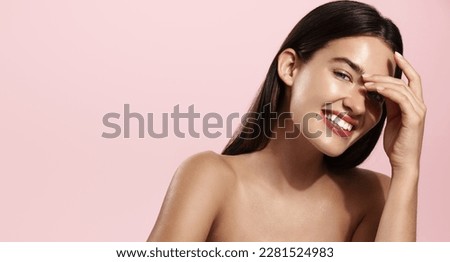 Skin care. Woman with beauty face touching healthy facial skin portrait. Beautiful smiling girl model with natural makeup touching glowing hydrated skin on pink background.