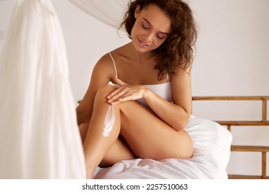 Skin Care Woman. Girl Applying Leg Cream. Beautiful Happy Lady Applying Cosmetic Moisturizing Lotion On Soft Silky Skin On White Bed. Beauty And Body Care 