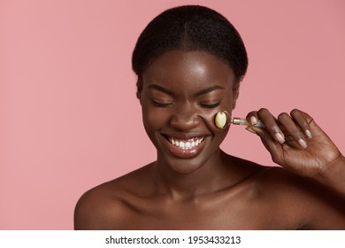 Skin care. Woman massage her face with jade roller. Smiling young woman with closed eyes. Isolated on pink background. 