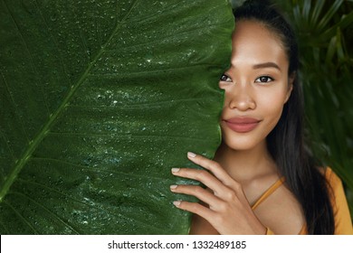 Skin Care. Woman Model With Beauty Face And Natural Green Leaf Plant. Portrait Of Beautiful Asian Girl With Nude Nails And Sexy Smile In Tropical Nature