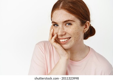Skin care. Young teenage redhead girl face without makeup, natural pale facial and white perfect smile, candid expression, touching cheek tenderly, cosmetics skincare routine effect