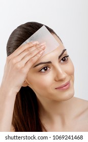 Skin care. Young woman removing oil from face using blotting papers. Photo of beautiful woman with smooth and healthy skin. Beauty concept
