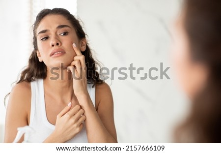 Skin Problem. Depressed Woman Touching Pimple On Face Looking At Mirror In Modern Bathroom. Facial Skin Issues, Medical Care And Treatment Concept. Selective Focus