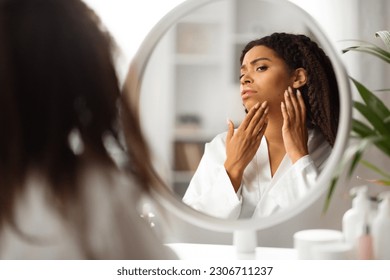 Skin Problems. Upset Young Black Woman Looking In Mirror At Pimple On Her Cheek, Worried African American Female Inspecting Her Face While Dong Skincare Routine, Suffering Acne, Selective Focus - Powered by Shutterstock