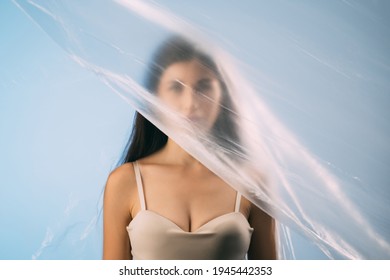 Skin Rejuvenation. Plastic Surgery. Body Enhancement. Art Portrait Of Woman Cleavage In Beige Lingerie Face Hidden Behind Wrinkled Texture Polyethylene Film Isolated On Blue Background.