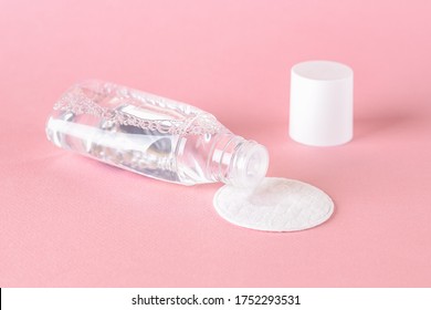 Skin tonic lotion or micellar water dripping from open bottle onto a cotton pad on a pastel pink background. Cosmetics for moisturizing and cleansing. Skin, hair or body care. Front view.