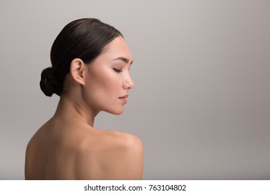 Skincare and beauty concept. Profile of charming serious young asian girl is looking down thoughtfully while demonstrating her perfect and fresh skin. Isolated background with copy space in right side