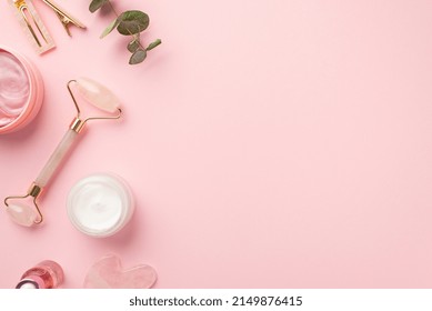 Skincare beauty concept. Top view photo of rose quartz roller gua sha pink eye patches cream jar glass bottle pink stylish barrettes and eucalyptus on pastel pink background with blank space
