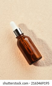 Skincare with beauty cosmetic face serum. Glass brown bottle with a pipette on a natural background with sand. Essential oil for moisturizing body skin. Copy space