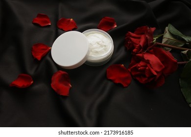 Skincare beauty treatment plant-based products with red rose petals. Jar of body or face moisturizer, homemade cosmetic ingredients on black fabric background. - Powered by Shutterstock