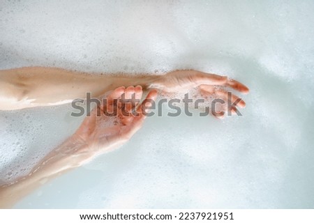 Skincare, bodycare and everyday beauty routine concepts. Top view of woman hands over hot water in bubble bath. Female holding arms together, making gentle touch to soft skin