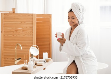 Skincare Cosmetics. Cheerful Millennial Lady Opening Moisturizing Jar Holding New Moisturizer Caring For Body Sitting On Bathtub In Modern Bathroom At Home. Spa And Wellness