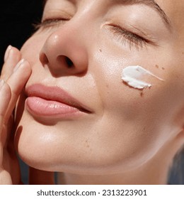 Skincare daily treatment. Beauty close up portrait of young woman with a healthy skin is applying a facial care product. Cream smear. 