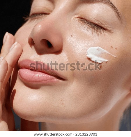 Skincare daily treatment. Beauty close up portrait of young woman with a healthy skin is applying a facial care product. Cream smear. 