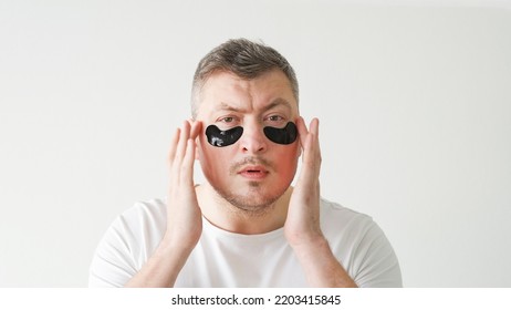 Skincare Procedure. Facial Treatment. Morning Routine. Metrosexual Man Applying Hydrogel Black Under Eye Patches On Light Background.