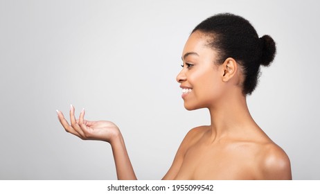 Skincare Product Advertisement. Happy Black Woman Holding Invisible Cosmetics Jar Or Bottle Advertising Product Looking Aside Over Gray Studio Background. Beauty Of Skin Concept. Panorama, Side View