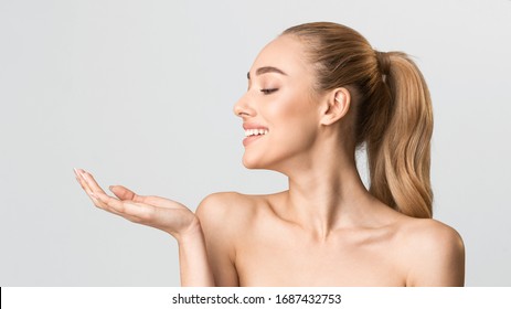 Skincare Product. Cheerful Girl Holding Invisible Object On Hand Posing On Gray Studio Background. Panorama