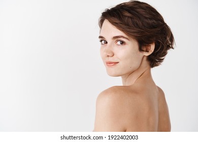 Skincare. Rear View Of Young Caucasian Woman Turn Head Back At Camera, Standing Half Naked On White Background And Smiling. Tender Girl With No Makeup And Natural Beauty.