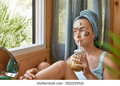 Skincare Routine. Middle Age Woman With Wrinkles And Hydrogel Under-eye Patches Drinking Smoothie And Looking In Window. Lifting Anti-wrinkle Mask Under Eyes. Skincare, Collagen Mask And Spa Concept.