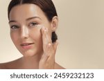 Skincare. Woman with beautiful face touching healthy facial skin portrait. Beautiful smiling Asian girl model with natural makeup enjoys glowing hydrated skin on beige background closeup. High-quality