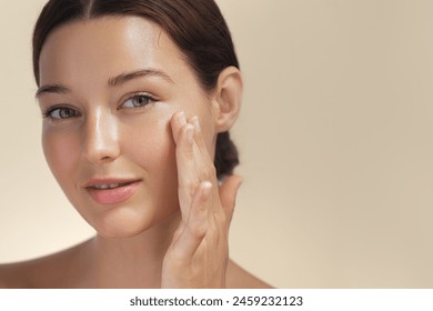 Skincare. Woman with beautiful face touching healthy facial skin portrait. Beautiful smiling Asian girl model with natural makeup enjoys glowing hydrated skin on beige background closeup. High-quality